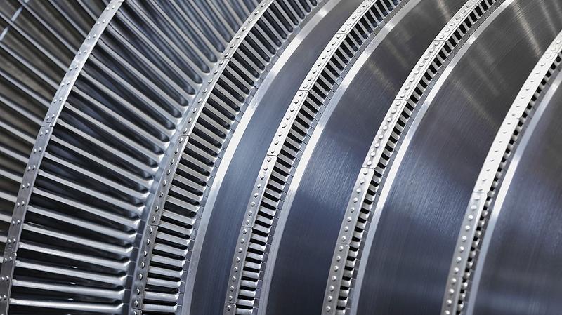 Nahaufnahme von mehreren metallenen Turbinenschaufeln, die spiralförmig angeordnet sind. Die Oberfläche ist glänzend und zeigt feine Rillen sowie präzise Befestigungsdetails. Die Struktur deutet auf eine komplexe technische Konstruktion hin.