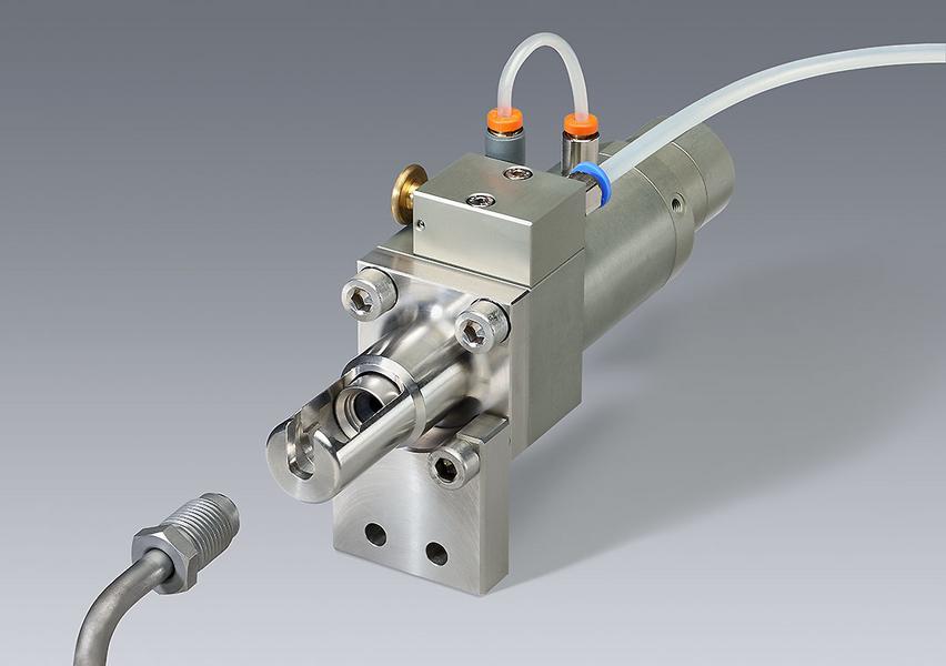 Anschluss Eine präzise Maschinenteileinheit, bestehend aus einem metallischen Gehäuse mit Anschlüssen und Schläuchen. Der Fokus liegt auf dem Ventilmechanismus, der für industrielle Anwendungen eingesetzt wird. Im Hintergrund ist eine neutrale graue Fläche.