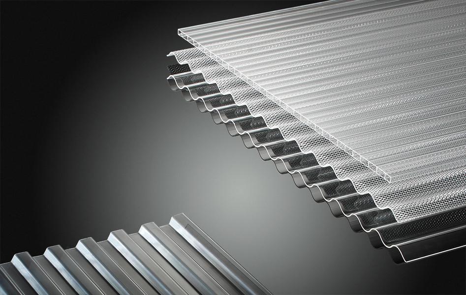 Acrylglas und Polycarbonat Eine Anordnung von transparenten, geriffelten Plexiglasplatten, die übereinander gestapelt sind. Die Platten unterscheiden sich in Struktur und Breite, wobei einige glatt und andere mit einem speziellen Muster versehen sind. Der Hintergrund ist dunkel.
