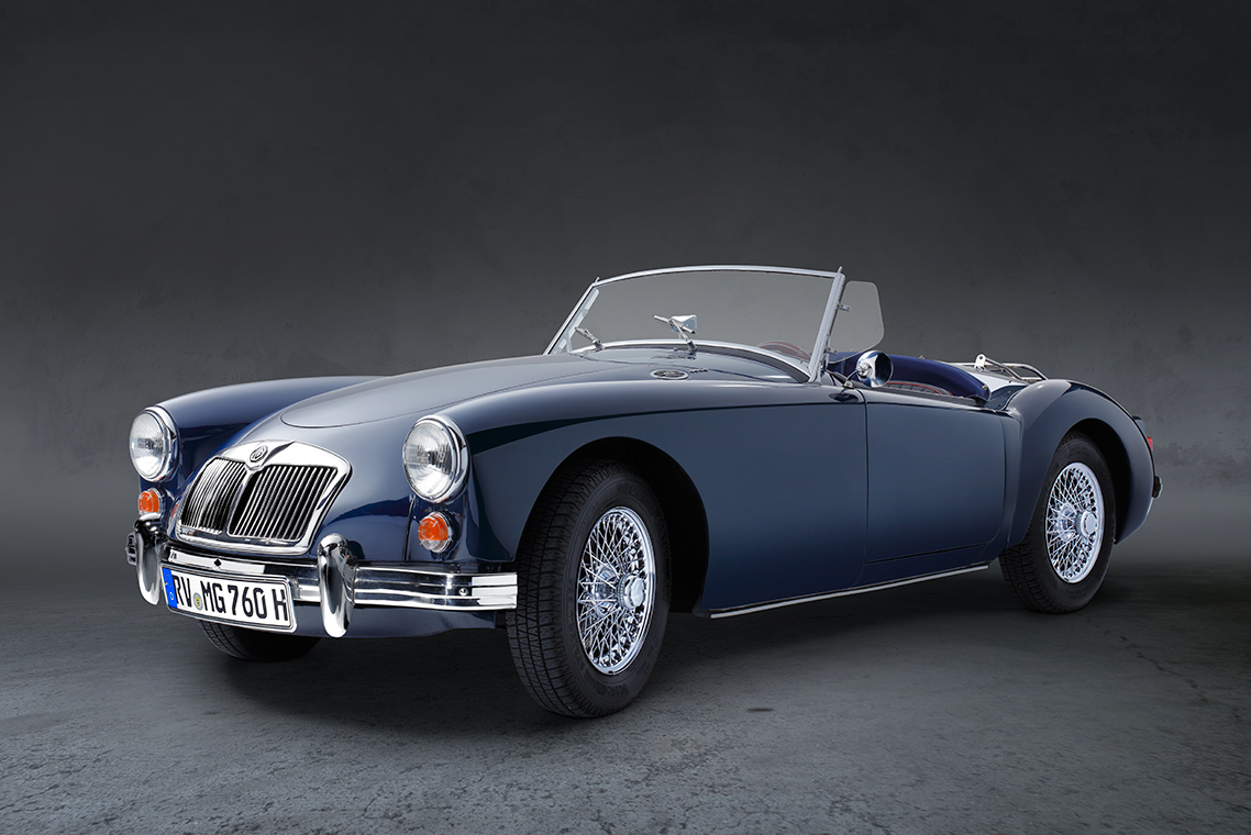 Ein blauer Oldtimer-Cabriolet mit offenem Verdeck steht auf einer neutralen, grauen Fläche. Die glänzenden Felgen und der Charme des klassischen Designs heben sich von der dunklen Hintergrundfarbe ab.