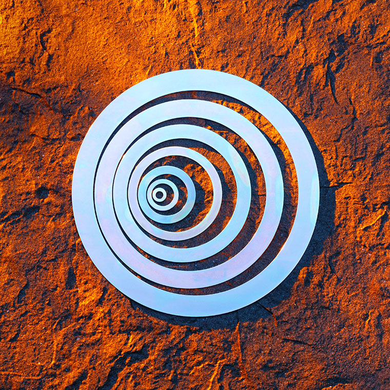 Unterlegscheiben Unterlegscheiben in verschiedenen Größen, das auf einer strukturierten, orangefarbenen Oberfläche platziert ist. Die Ringe sind in einem hellen, glänzenden Material gehalten, das Licht reflektiert.